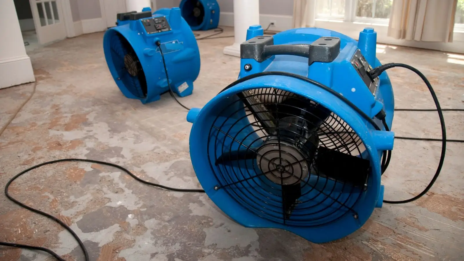 Large blue air mover running on a damp floor during flood damage drying